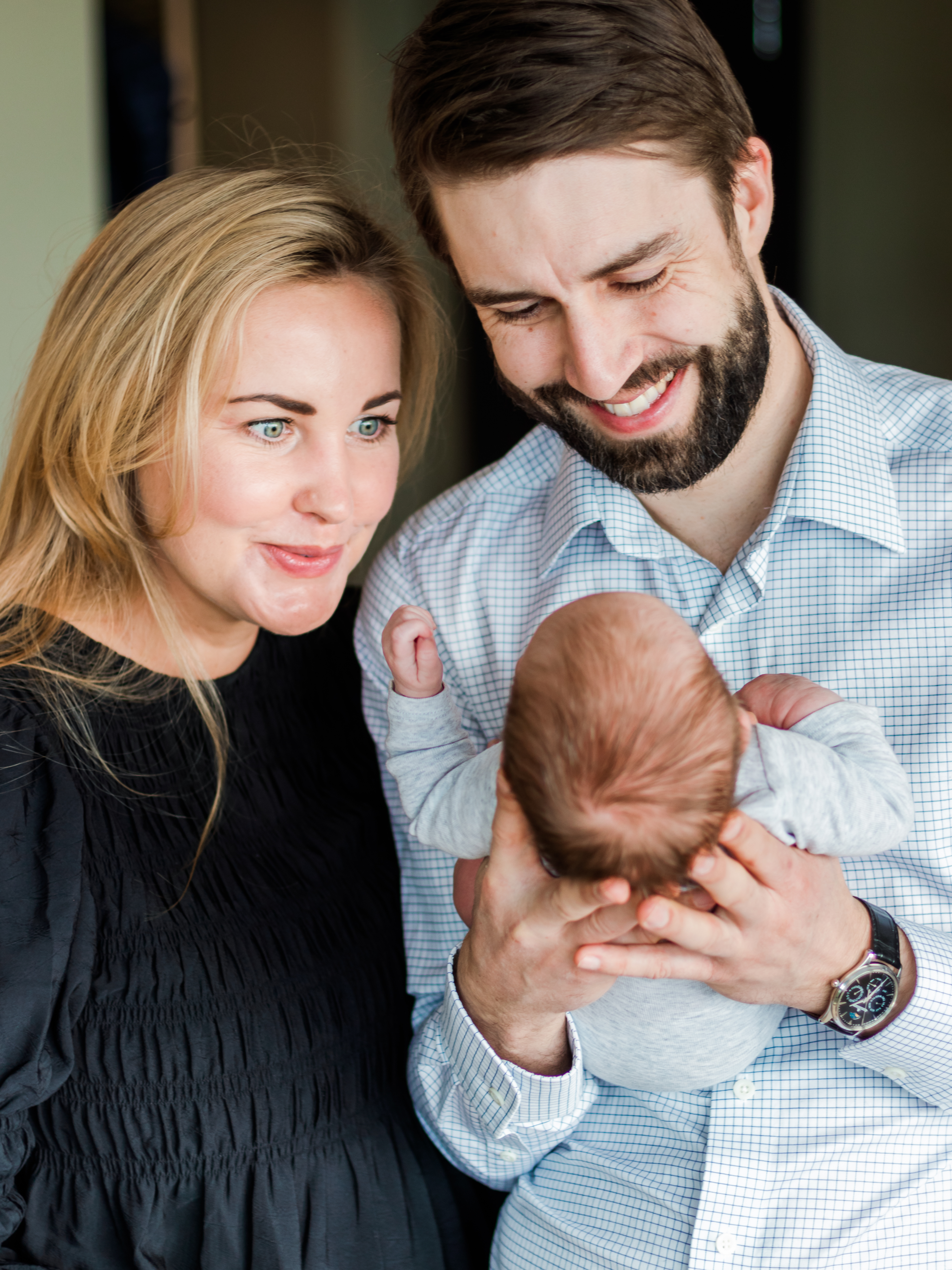 Dad smiling at infant in hands, mom making silly face, lifestyle photography